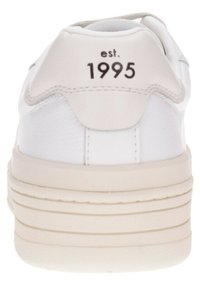 Baskets blanches avec un matériau texturé, un talon arrondi et une languette lisse. Présente "est. 1995" imprimé à l'arrière. Semelle beige solide.