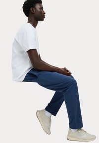 Witte t-shirt met korte mouwen, blauwe sweatpants en beige sportschoenen. Zitpositie, focus op materialen en kleurcontrast.