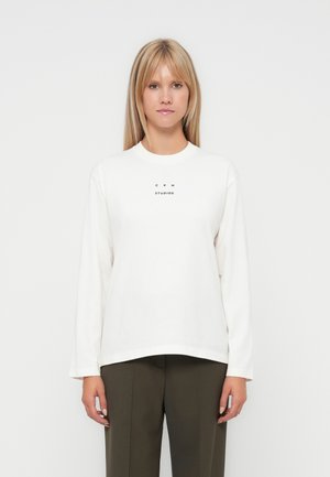 Vit långärmad sweatshirt med ribbad rundad halsringning och tryckt logo i svart på bröstet. Mjuk tyg, avslappnad passform och rak nederkant.