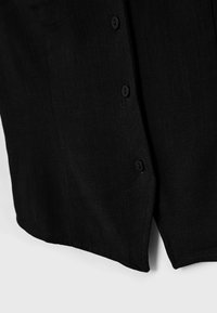 Close-up of black fabric with three matching black buttons vertically aligned and a small side slit at the bottom edge.
