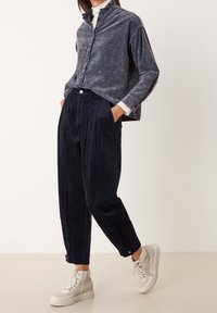 Outfit casual composto da una camicia blu navy sbiadita con bottoni, pantaloni di velluto a coste blu scuro con texture e sneakers alte beige.