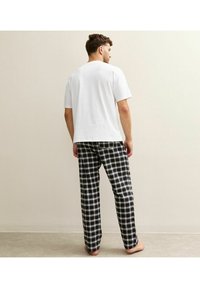 White short-sleeve shirt with relaxed fit, paired with black and white plaid pajama pants made of soft fabric, featuring straight legs and no pockets.