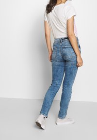 Ljusblå denimjeans med en figurnära design, med bakfickor och sömnadsdetaljer. Kombinerat med en enkel vit skjorta och vita sneakers.