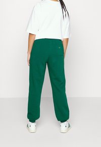 Zelené tepláky s elastickým pasem a manžetami na nohavicích. Na zadní kapse je malé logo. Kombinováno s bílým oversized tričkem.