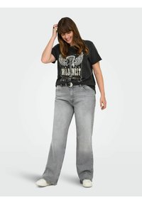 Sivi jeans s prostranim krojem, upareni s crnom majicom s grafikom koja prikazuje slona i krila. Bele patike upotpunjuju outfit.