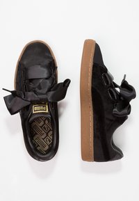 Černé tenisky vyrobené z hladkých a strukturovaných materiálů, s oversized saténovými tkaničkami, hnědou gumovou podrážkou a vzorovaným interiérem.