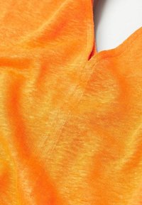 Gros plan sur un tissu orange doux avec des coutures visibles et un léger pli, montrant la texture et les détails du tissage.
