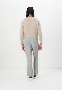 Beige langærmet trøje parret med lysegrå bukser. Bukserne har lige snit med baglommer og en glat tekstur. Hvide sneakers inkluderet.