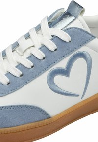 Zapatilla blanca con paneles de ante azul claro, un logo de corazón bordado en azul, cordones blancos y un acento azul brillante en el talón.