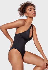 Bañador negro de una sola pieza con diseño de un hombro, textura suave y corte lateral curvado. Presenta un estilo minimalista y un acabado liso.