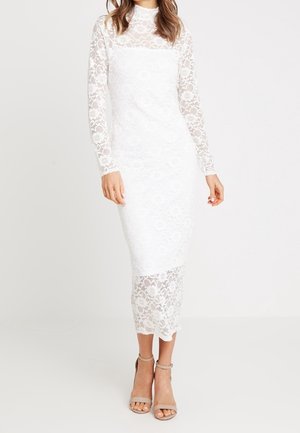 Abito bianco in pizzo con maniche lunghe, design aderente e motivi floreali. Lunghezza midi con orlo scalloppato. Indossato con tacchi a strap beige.