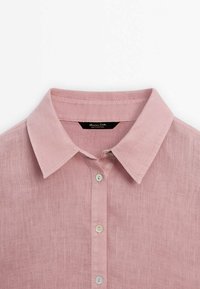 Chemise en lin rose avec col pointu et trois boutons visibles sur le devant, présentée sur fond blanc.