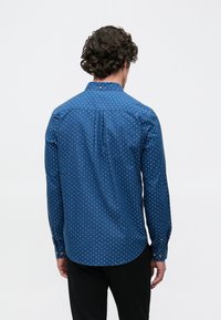 Sinine nööbitav särk, millel on täpiline muster, pikad varrukad, krae ja kumer serv. Valmistatud siledast kangast, millel on kerge läige.