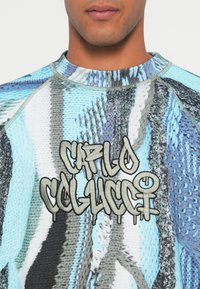 Texturerad tröja med ett blått och grått abstrakt mönster, med en framträdande svart och grå broderad logotyp i mitten.