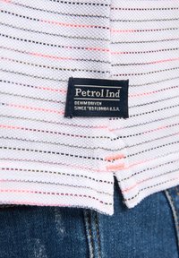 Pruhovaná látka v bílé, šedé a růžové barvě; obsahuje černou etiketu s textem "Petrol Ind" a "DENIM DRIVEN"; ležérní design.