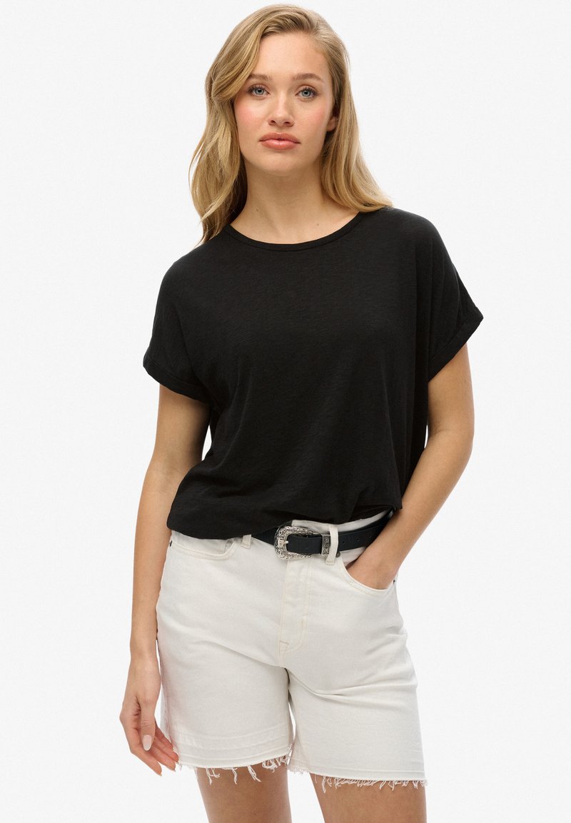 Zwarte T-shirt met korte mouwen en een relaxte pasvorm, gecombineerd met witte denim shorts met rafelige randen en een zwarte riem met een zilveren gesp.
