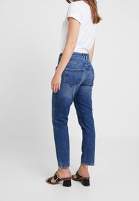 Modré džíny z denimu se střihem rovné nohavice, středně vysokým pasem a bledou texturou. Kombinované s černými sandály na blokovém podpatku a bílým tričkem.