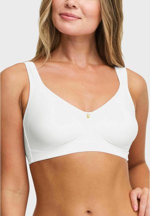 Vrouw draagt een witte draadloze BH met brede bandjes en een klein gouden embleem in het midden, zichtbaar van nek tot taille.
