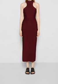 Burgundská maxi šaty s řaseným halter výstřihem a těsným střihem. Nosit s černými sandály na plochém podpatku s pásky. Jednoduchý design, jemná textura.