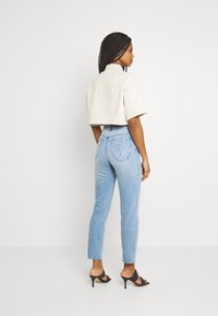 Camisa bege corta, calças de ganga de cintura alta azul claro com um design de bolso traseiro em forma de coração e sandálias pretas de salto alto. Texturas suaves, estilo casual.