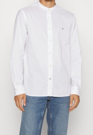 Camicia bianca a maniche lunghe con colletto alla coreana, chiusura con bottoni frontale e piccolo dettaglio del logo sul lato sinistro del petto. Tessuto di cotone liscio.
