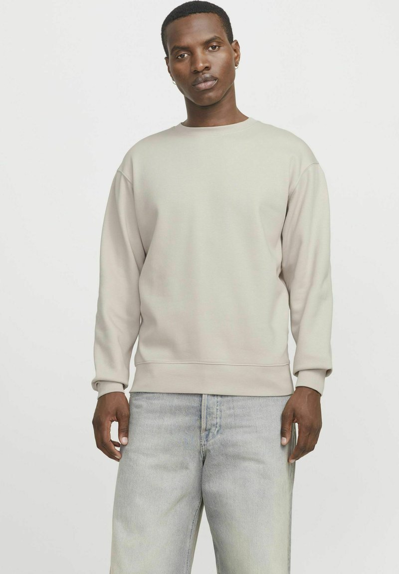 Lichtgrijze sweatshirt van zachte stof, met een ronde halslijn en ribgebreide manchetten, gecombineerd met vervaagde lichtblauwe jeans.