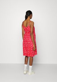 Abito floreale rosso con spalline sottili e orlo fino al ginocchio. Presenta un corpetto aderente e una gonna fluida. Indossato con calzini bianchi e sneakers.