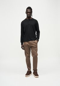 Chemise henley noire à manches longues, pantalon marron à coupe décontractée, et baskets marron avec semelles blanches. Design minimaliste, textures lisses.