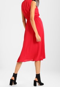 Rode mouwloze midi-jurk met een geplooide taille en een vloeiende rok, gemaakt van lichtgewicht stof; gecombineerd met zwarte enkellaarsjes met hak.