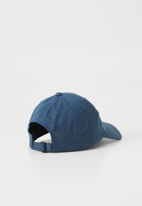 Blue denim baseball cap with a curved brim, adjustable strap at the back, and six ventilation eyelets. Textured surface and soft fabric.