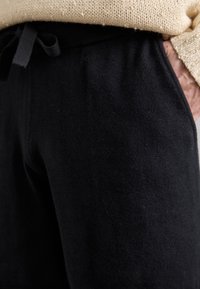 Sorte sweatpants lavet af blødt stof, med elastisk talje med snoretræk og sidelommer. Nærbillede fremhæver teksturen.