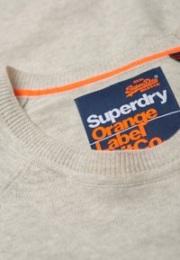 Felpa grigia con scollatura a coste, caratterizzata da un'etichetta blu e arancione con la scritta "Superdry Orange Label." Tessuto morbido con una texture liscia.