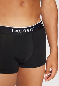 Fekete boxer alsónadrág, puha anyagból készült. Széles derékrészen fehér díszítéssel ellátott LACOSTE logóval. Kellemesen testhezálló dizájn, sima textúra.