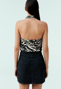 Haut halter à imprimé zèbre noir et blanc associé à une mini-jupe en denim foncé avec deux poches à l'arrière et un ourlet droit.