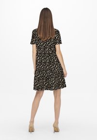 Vestito nero a fiori con maniche corte, vita arricciata e gonna al ginocchio. Presenta motivi floreali bianchi e una vestibilità comoda. Tacchi color nude.