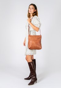 Tan leather shoulder bag with a smooth texture and minimalist design. The bag features a long strap and a soft, unstructured shape.