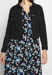 Czarna, krótka kurtka dżinsowa z przodem zapinanym na guziki i dwoma kieszeniami na piersi, nałożona na czarną sukienkę w kwiaty z niebieskimi i różowymi motywami.