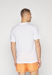Camiseta de algodón blanca con mangas cortas, cuello redondo y una textura suave, combinada con pantalones cortos naranjas texturizados que cuentan con acentos reflectantes.