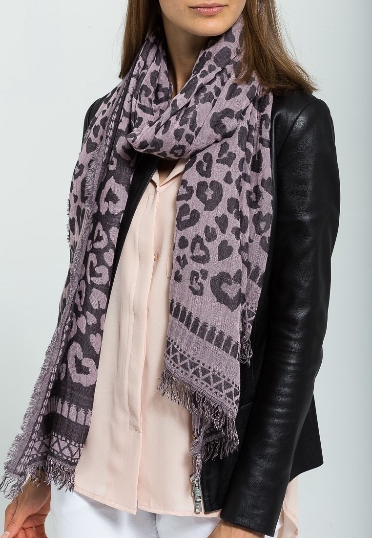 Femme portant un chemisier rose clair, une veste en cuir noire et une grande écharpe violette à imprimé léopard avec des bords frangés.