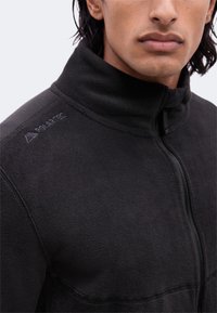 Κοντινό πλάνο ενός ατόμου που φοράει μαύρο fleece μπουφάν Polartec με ψηλό γιακά και φερμουάρ μπροστά.