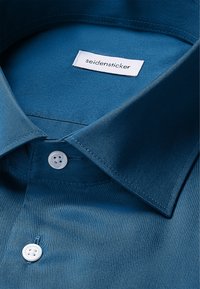 Morski satynowy shirt z sztywnym kołnierzykiem, z białą metką oznaczoną "seidensticker" oraz dwoma białymi plastikowymi guzikami na listwie.