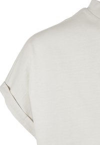 Chemise beige clair en mélange de coton avec une coupe décontractée, manches courtes retroussées et texture lisse. Design simple et minimaliste.