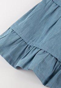 Helles blaues Chambray-Kleid mit Rüschenschichten, weichem Stoff und sauberen Nähten. Der Stoff wirkt leicht und atmungsaktiv.