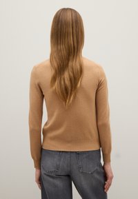 Maglione beige in cashmere con polsini e orlo a coste, design aderente, mostrato di spalle con jeans in denim grigio dritti e capelli lunghi e lisci.