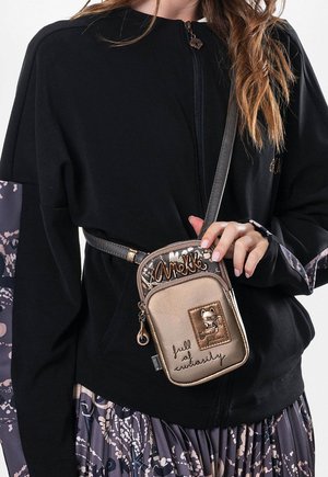 Schwarze Zip-Jacke mit langen Ärmeln, kombiniert mit einer kleinen beigen Umhängetasche mit Katzenmotiv und handgeschriebenen Akzenten.