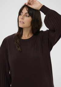 Bruine lange mouwtrui met een gladde body en geplooide, getextureerde mouwen. Ronde halslijn, casual pasvorm en zachte stof.