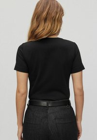 Czarny t-shirt z krótkim rękawem o klasycznym okrągłym dekolcie, wykonany z miękkiej bawełny, w połączeniu z ciemnoniebieskimi dżinsami i cienkim czarnym paskiem.