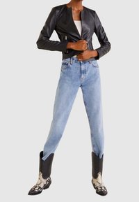 Černá kožená zkrácená bunda, modré džíny s vysokým pasem a černobílé kostkované kovbojské boty s špičatými špičkami.