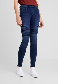 Vaqueros de pitillo de tiro alto en azul marino con detalles acanalados en las rodillas, hechos de material vaquero, con cremallera y bolsillos frontales.