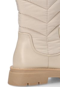 Botín beige hasta el tobillo con textura acolchada, material de cuero suave, punta redonda y suela gruesa de color marrón claro. Los acentos laterales incluyen detalles de costura.